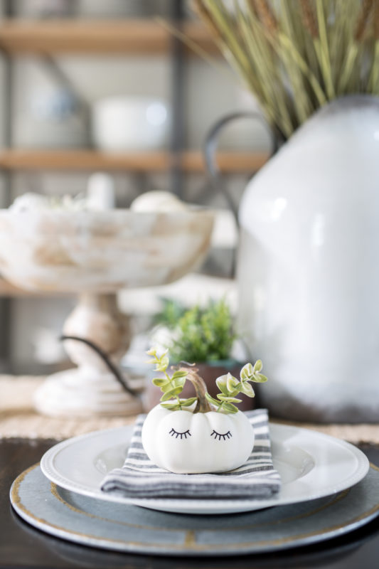 Little white pumpkins with eyelashes painted on sitting on the white plates on table.