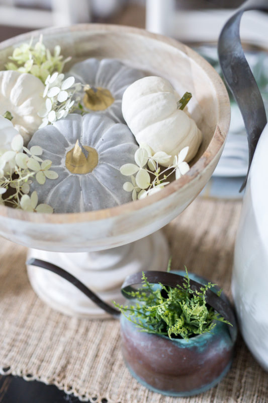 Pedestal bowl filled with neutral little pumpkins on the table.