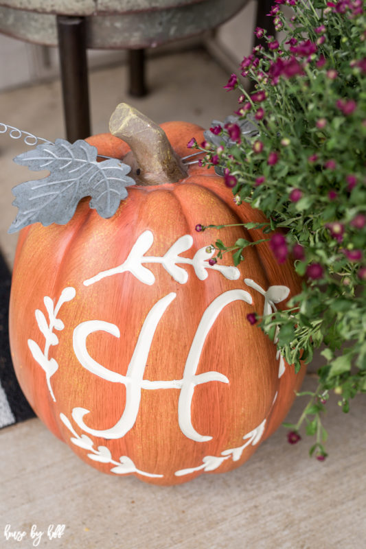 Monogramed orange pumpkin with purple flowers beside it.