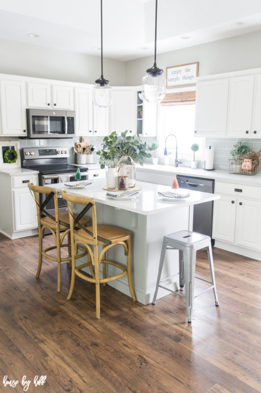 A mostly white kitchen with an island and two chairs.