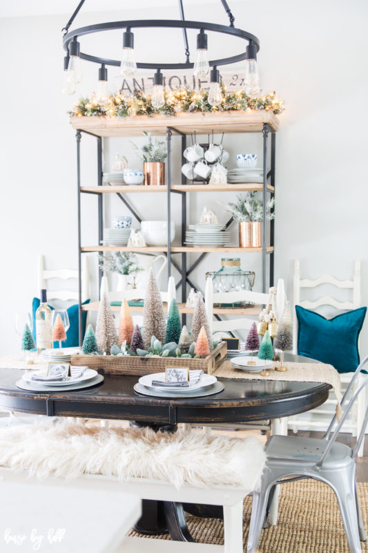 A colorful holiday dining room with teal pillows, faux white fur on the bench and multi colored mini Christmas trees as a centerpiece.