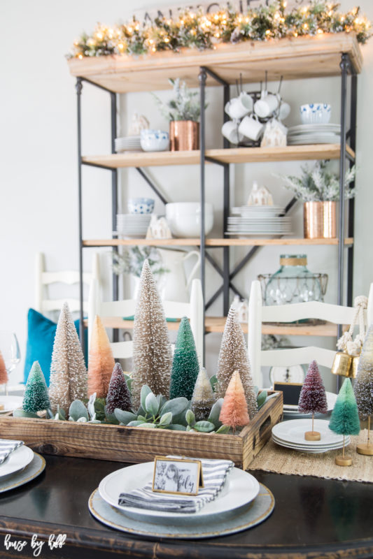 Mini trees on a wooden tray with succulents on the dining room table, and open shelving with lights on it.