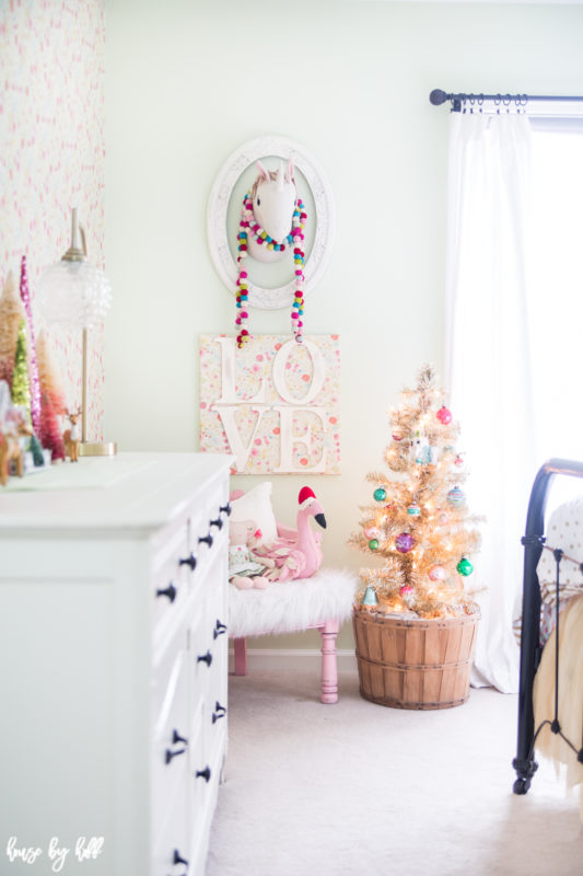A sweet and colorful holiday little girl's room with a unicorn on the wall, a decorated Christmas tree in the corner and mini trees on the dresser.