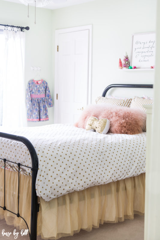 Little girl's bed and dress hanging by the window.