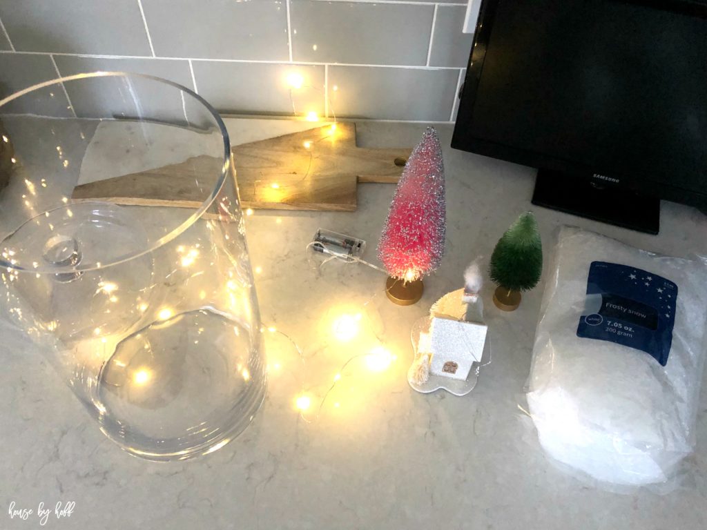 A clear glass jar with mini trees beside it and cotton on the kitchen counter.