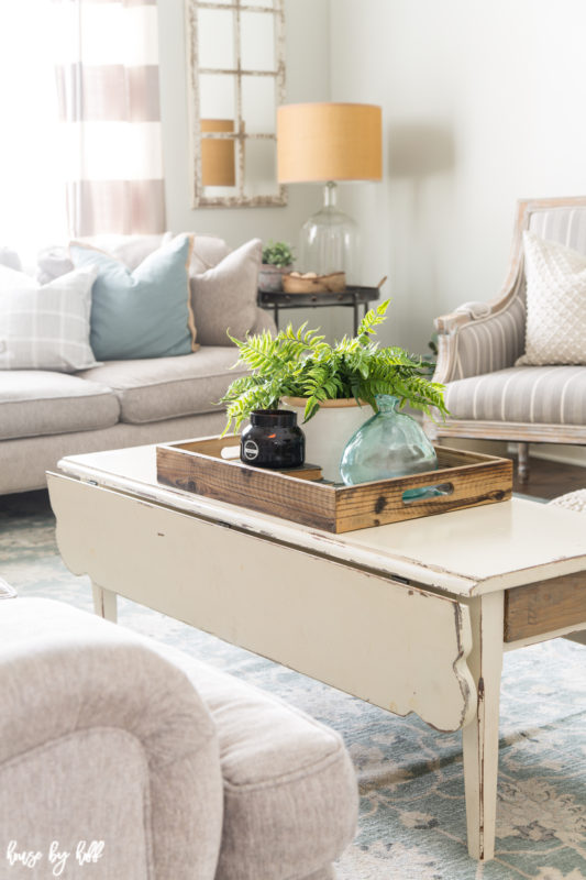 A wooden distressed coffee table with a wooden tray and a green fern.