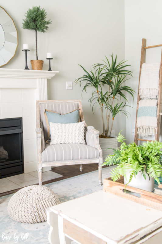 A soft striped neutral chair is in the corner of the room beside the fireplace.