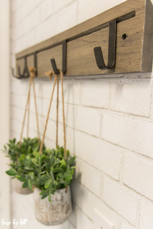 A wooden bar with metal hooks on the wall and plants hanging on the hooks.