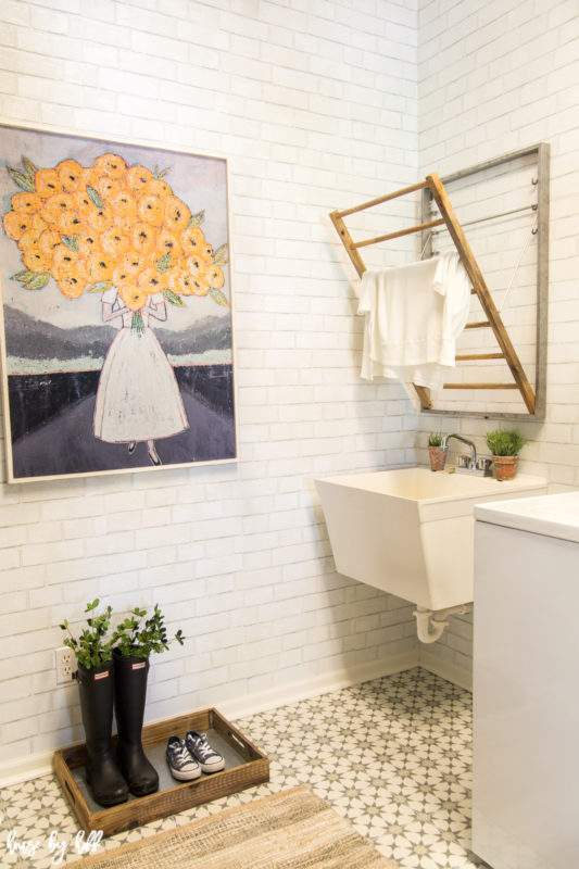 A small mudroom with neutral walls, boots on the floor and a small sink.