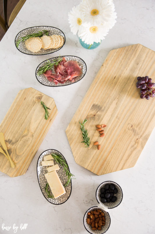 White daisies, olives, cheese, meat and grapes all beside the charcuterie board.