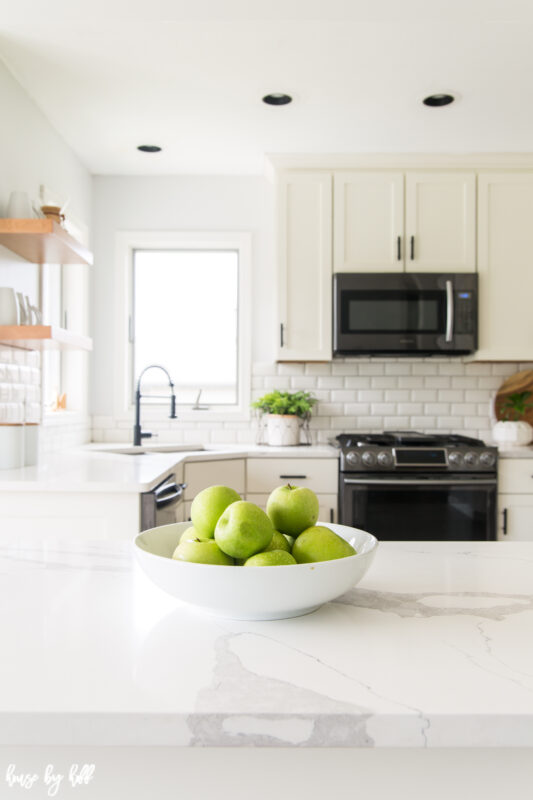 There is a white bowl full of green apples on the counter.