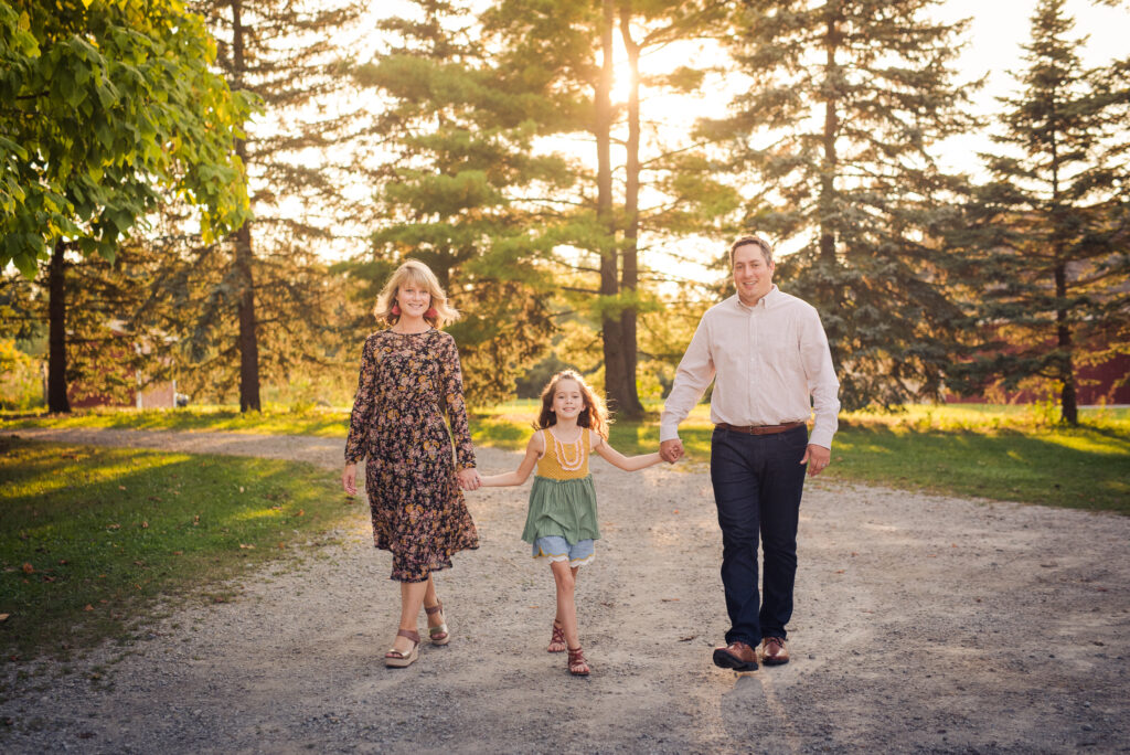 The family of three walking down a road lined by trees.