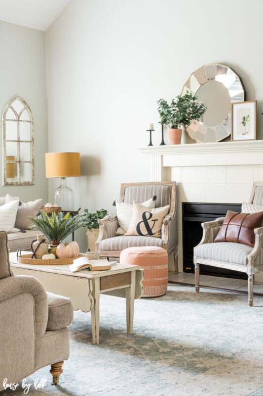 Blush colors are in the living room with a wooden coffee table, white fireplace and a large round mirror on the mantel.