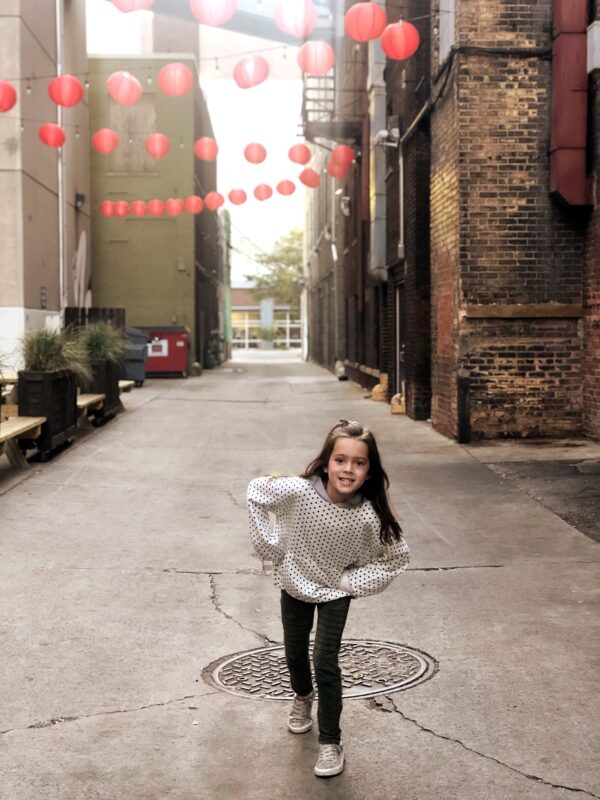 A picture of a little girl in an alley with red patio lanterns strung up.