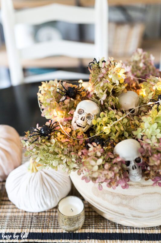 There is a bowl filled with hydrangea in pink and green, with skulls and spiders intertwined.