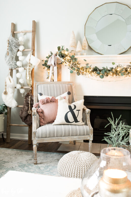 There is an armchair beside the fireplace with neutral and pink throw pillows on the chair.