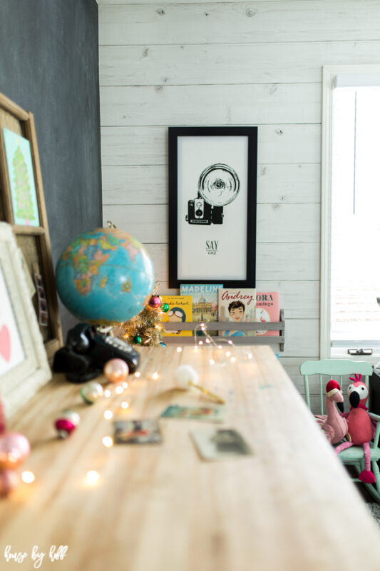 There is a black and white old fashioned camera photo on the wood planked wall that is whitewashed.