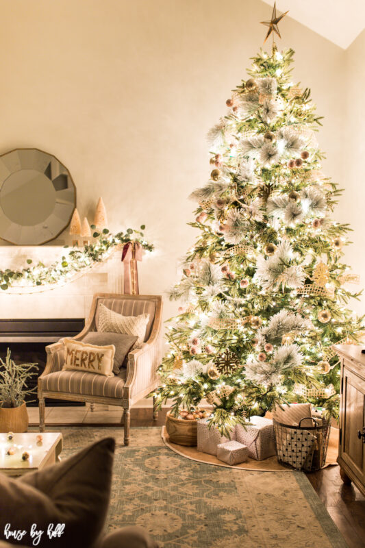 There is a MERRY throw pillow on a chair beside the tree.