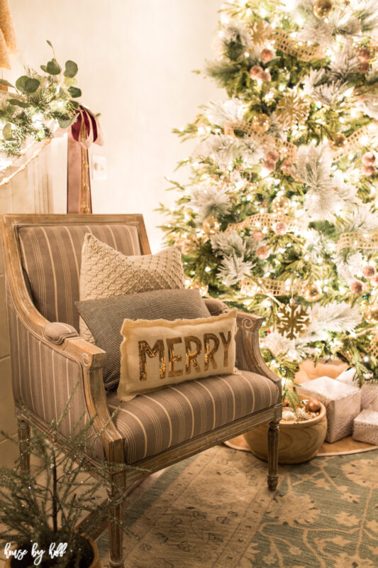 A neutral armchair is beside the tree with throw pillows on it.