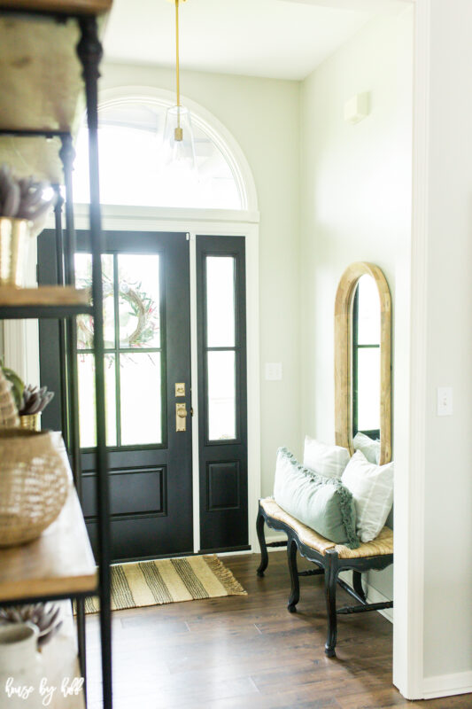 A mirror hangs on the wall by the front door of the house.