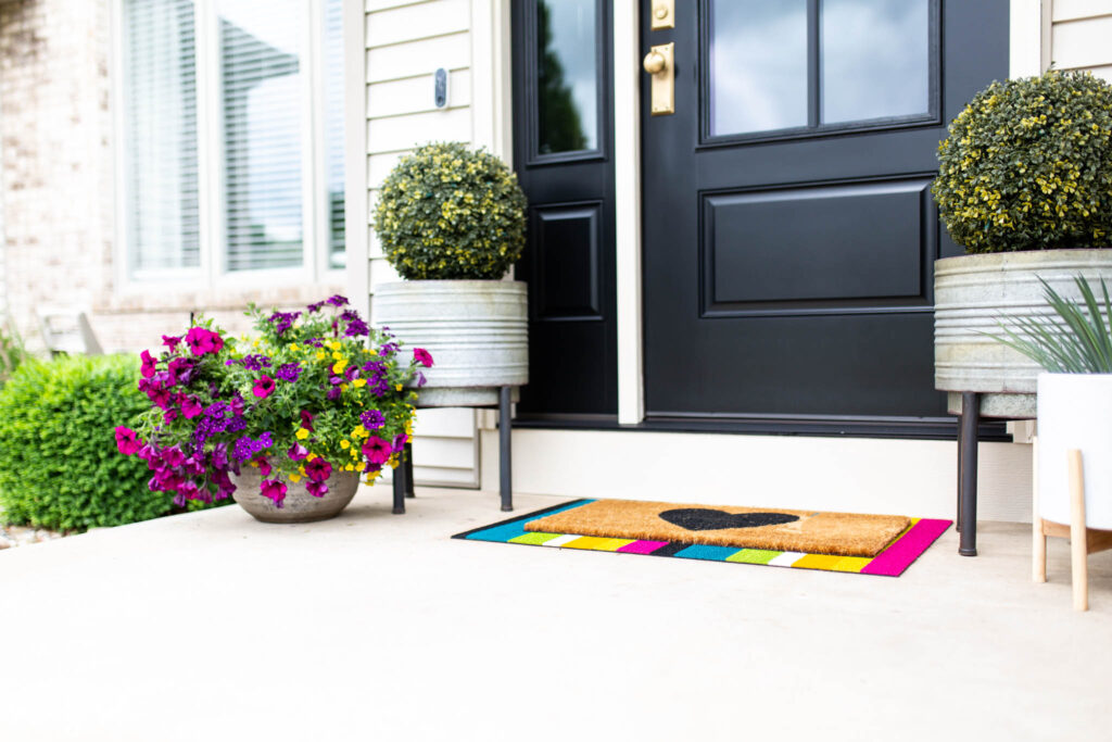 Colorful striped front door mat and flowers on porch